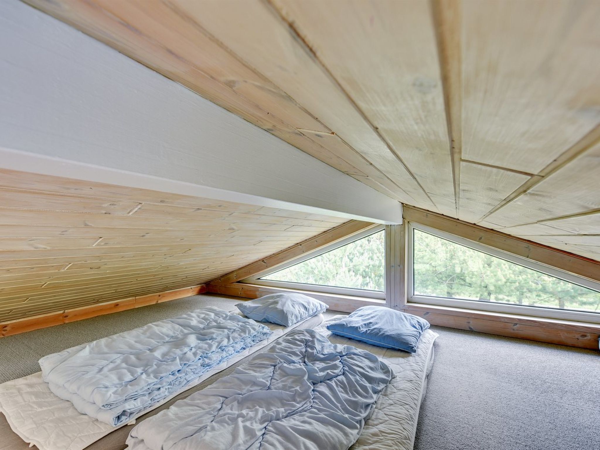 A bedroom with a sloped ceiling, two beds with blue bedding, and large windows.