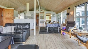 A spacious living area with a wooden floor, a black leather sofa, a dining table with chairs, and a large window providing natural light. - "Rudy" - 900m to the fjord by Interhome (Blåvand)