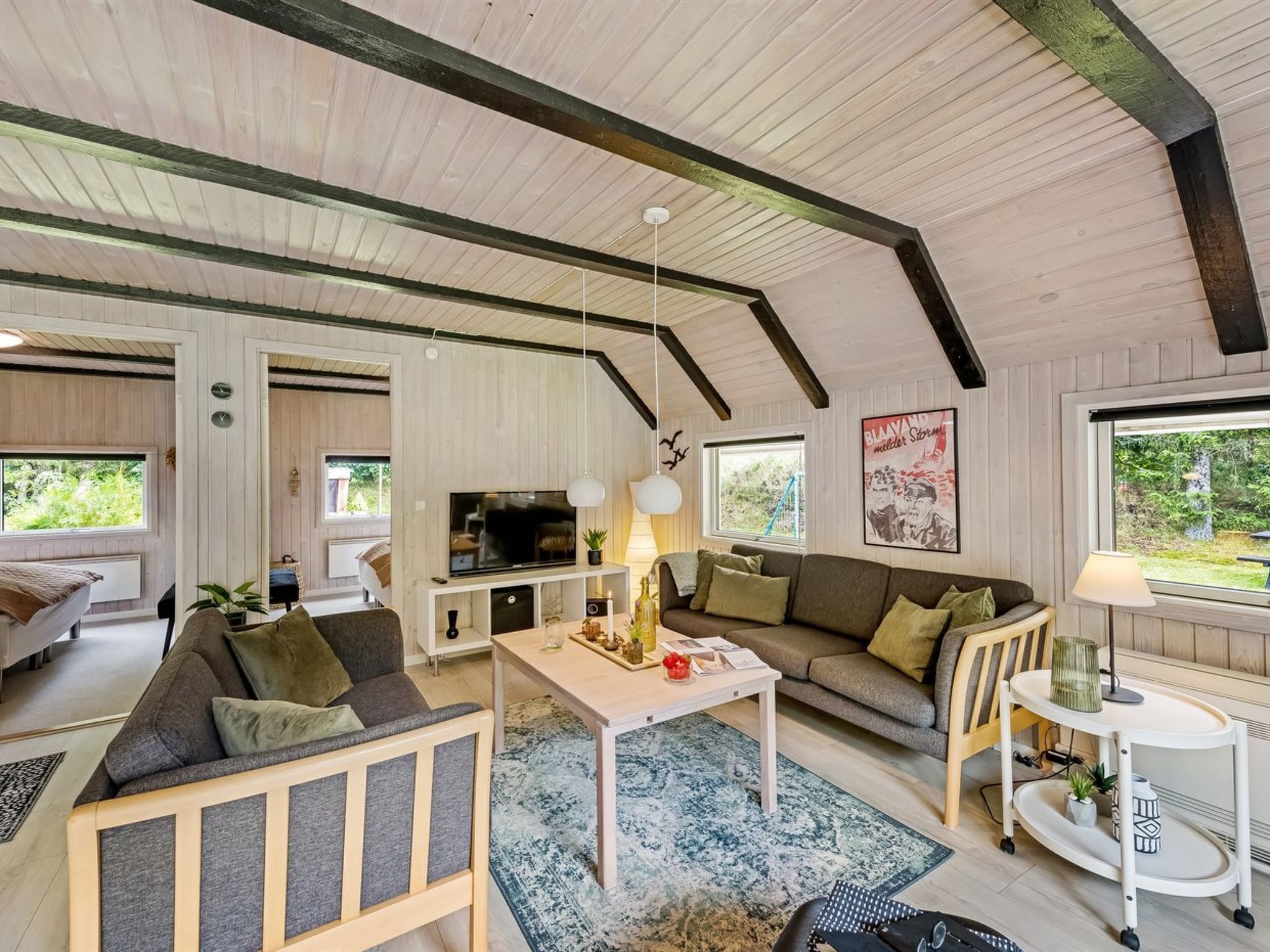 A spacious living area with a high ceiling, wooden beams, a large TV, a sofa, a coffee table, and a dining table.