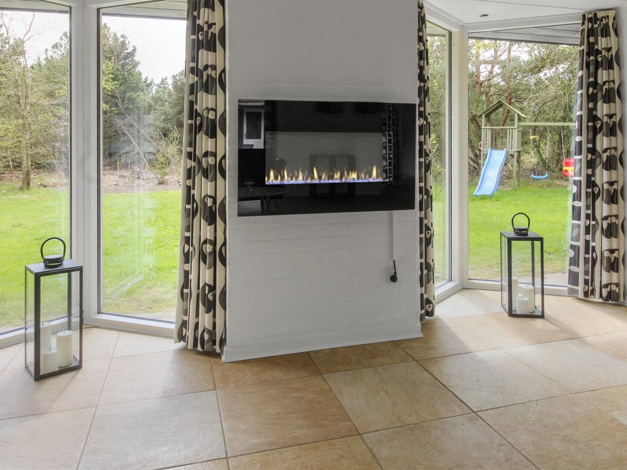 Een moderne woonkamer met een open haard, grote ramen en uitzicht op een tuin.