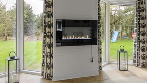 A modern living room with a fireplace, large windows, and a view of a garden.
