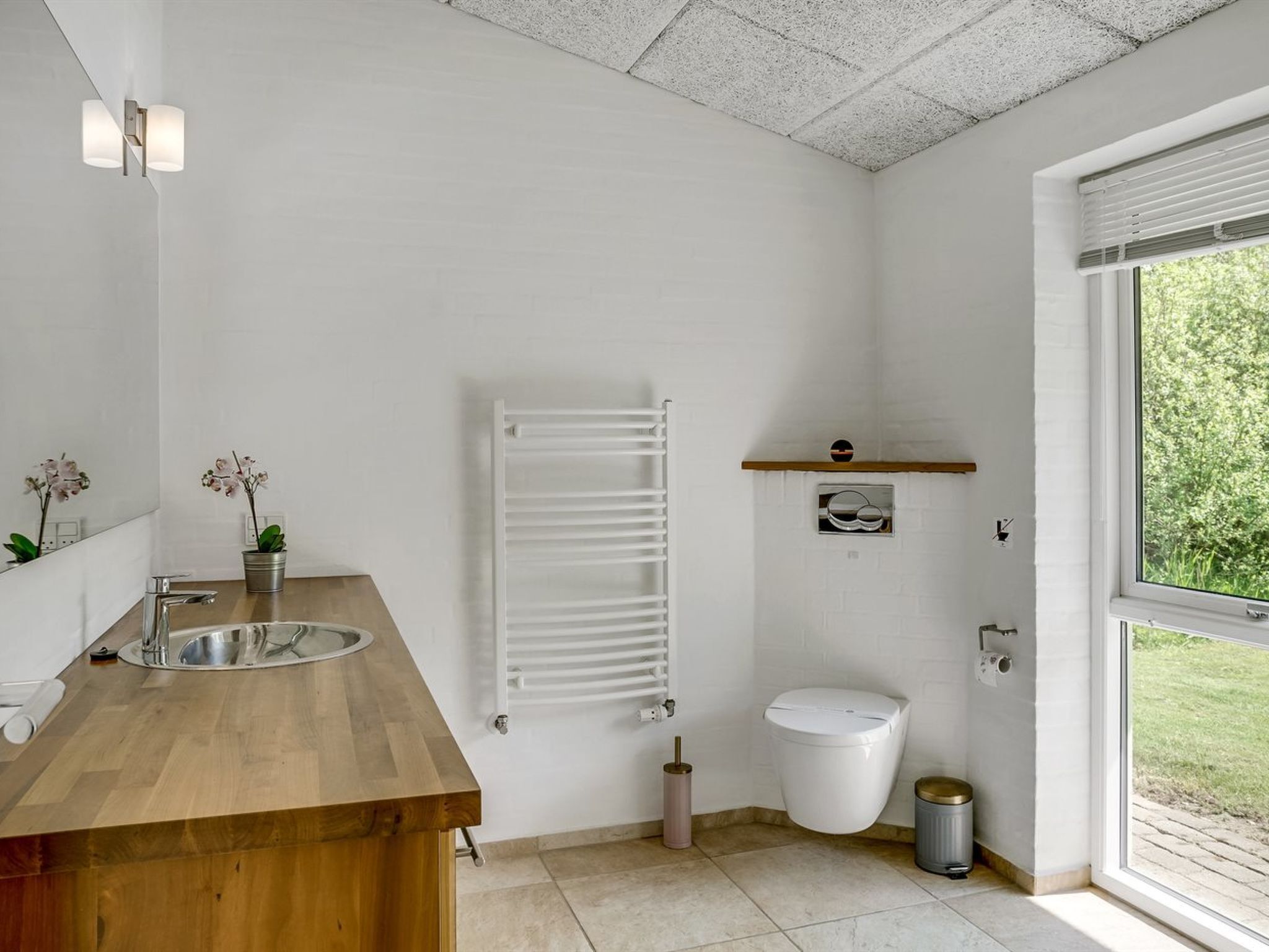 Een moderne badkamer met een houten wastafel, een wit toilet, een handdoekhouder en een raam met uitzicht op groen.