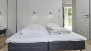 A double bed with a white duvet and two pillows, a bedside table, and a wall-mounted light fixture.