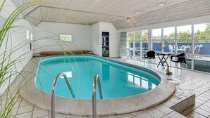 An indoor swimming pool with a wooden ceiling, a lounge area with a table and chairs, and a view of the outdoors through large windows. - "Madalena" - 2.8km from the sea by Interhome (Rømø)