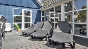 A covered outdoor area with lounge chairs, a table, and a large window overlooking a blue building. - "Madalena" - 2.8km from the sea by Interhome (Rømø)