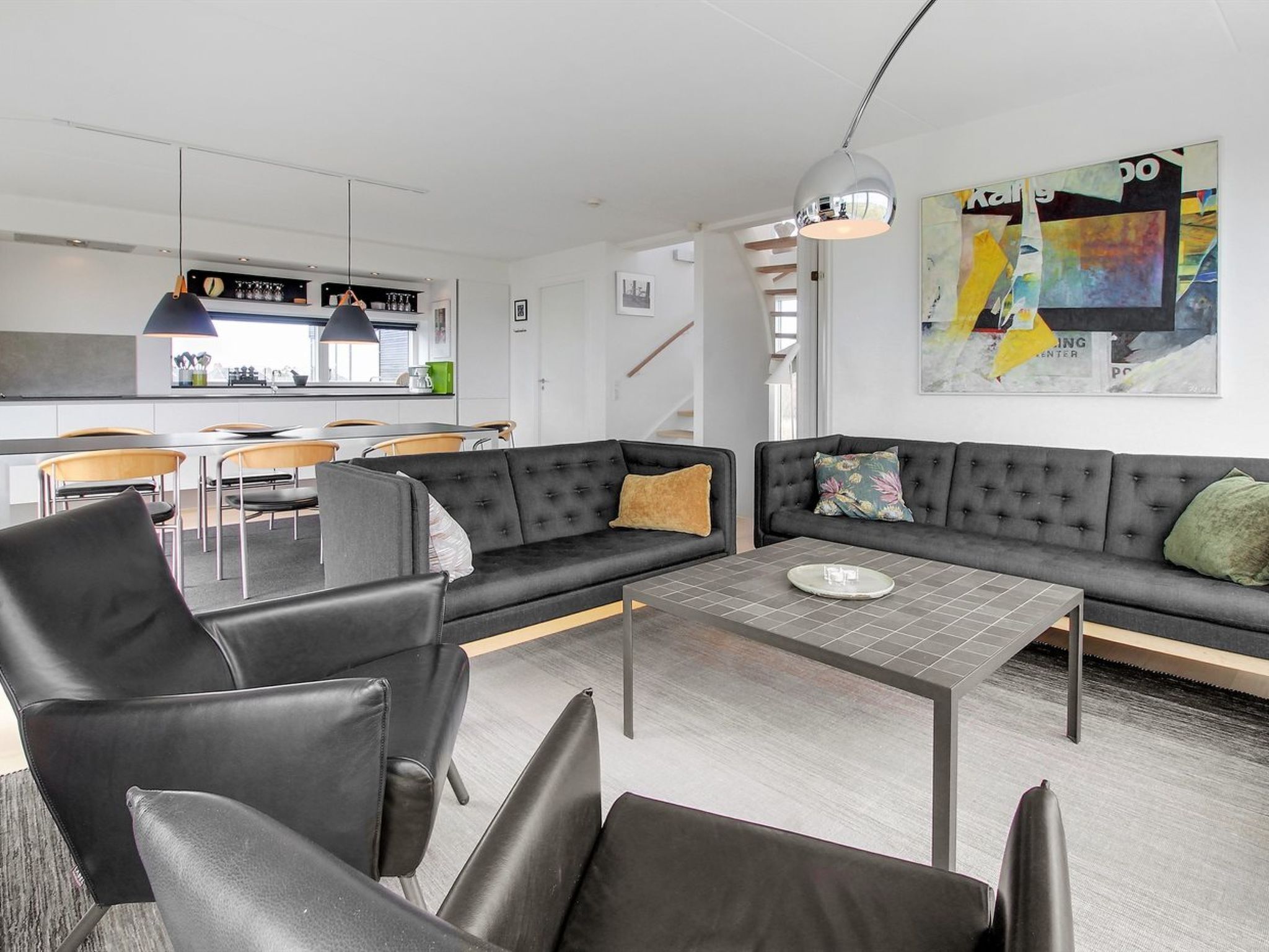 Una sala de estar moderna con un sofá, sillas, una mesa de centro y una cocina al fondo.