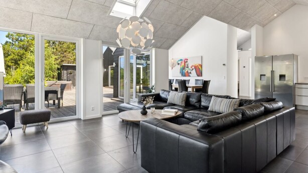 Un salon moderne avec un canapé en cuir noir, une table basse ronde et une grande fenêtre donnant sur une terrasse.