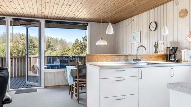 Une cuisine moderne avec un plafond en bois, un grand îlot central doté d’un évier et une vue sur une terrasse extérieure, accessible par une porte vitrée.