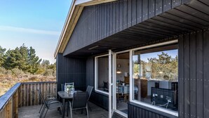 Une terrasse extérieure moderne dotée d’un espace repas, de grandes fenêtres et offrant une vue sur le paysage environnant.