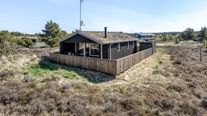 Une cabane moderne dotée d’une grande terrasse, entourée d’un paysage naturel.