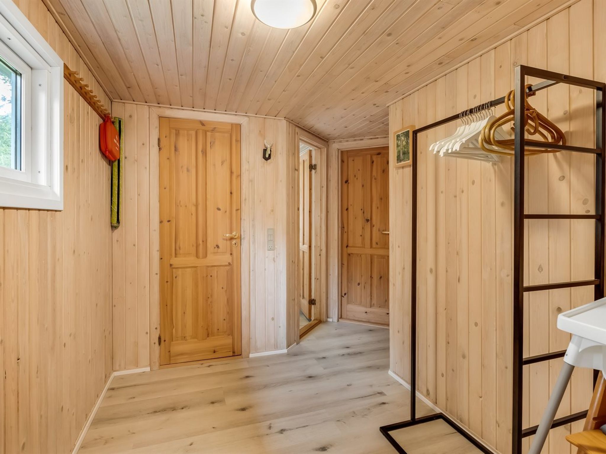 A wooden interior hallway with a wooden door, a coat rack, and a white table.