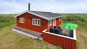 Et rødt træhus med skorsten, terrasse og en grøn parasol.