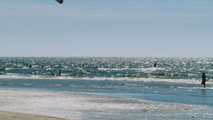 En strand med folk, der bader, og en kitesurfer i luften.