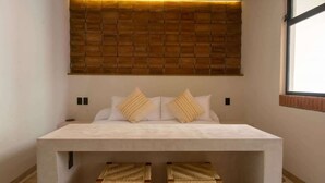 A modern bedroom with a large bed, two woven stools, a wooden headboard, and a window.