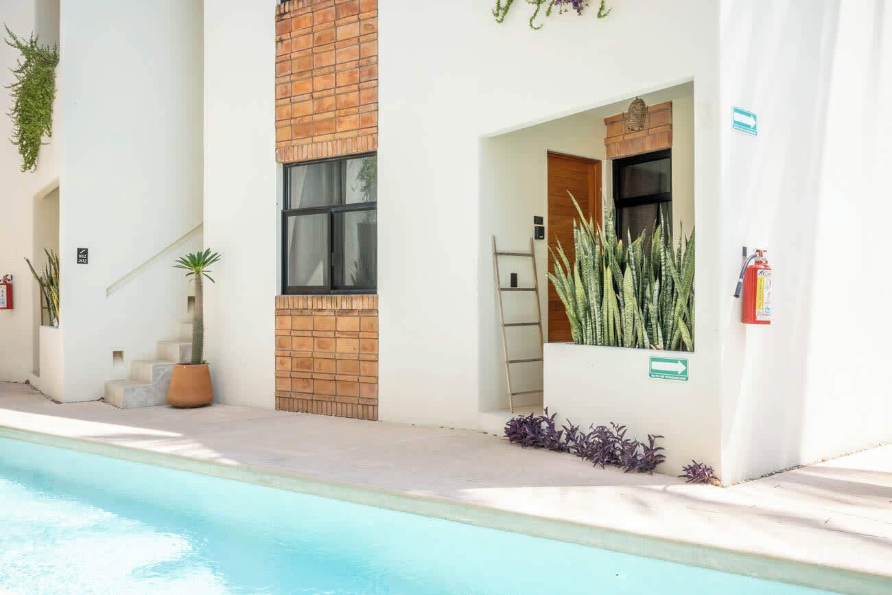 Un espace aménagé au bord de la piscine, avec un mur en briques, une porte en bois et des plantes en pot.