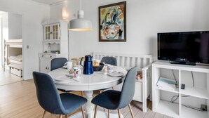 A modern, well-lit dining area with a round table, blue chairs, and a white cabinet with glass doors.