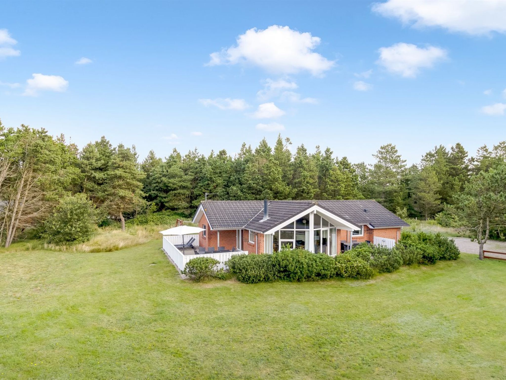A single-story house with a sloped roof, surrounded by a well-maintained lawn and dense forest.