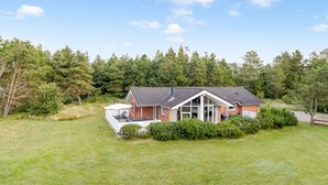 A single-story house with a sloped roof, surrounded by a well-maintained lawn and dense forest.