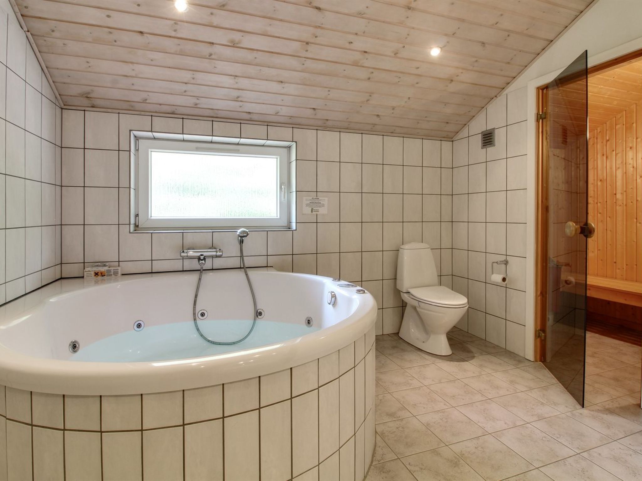 A modern bathroom with a freestanding bathtub, a toilet, and a window providing natural light.