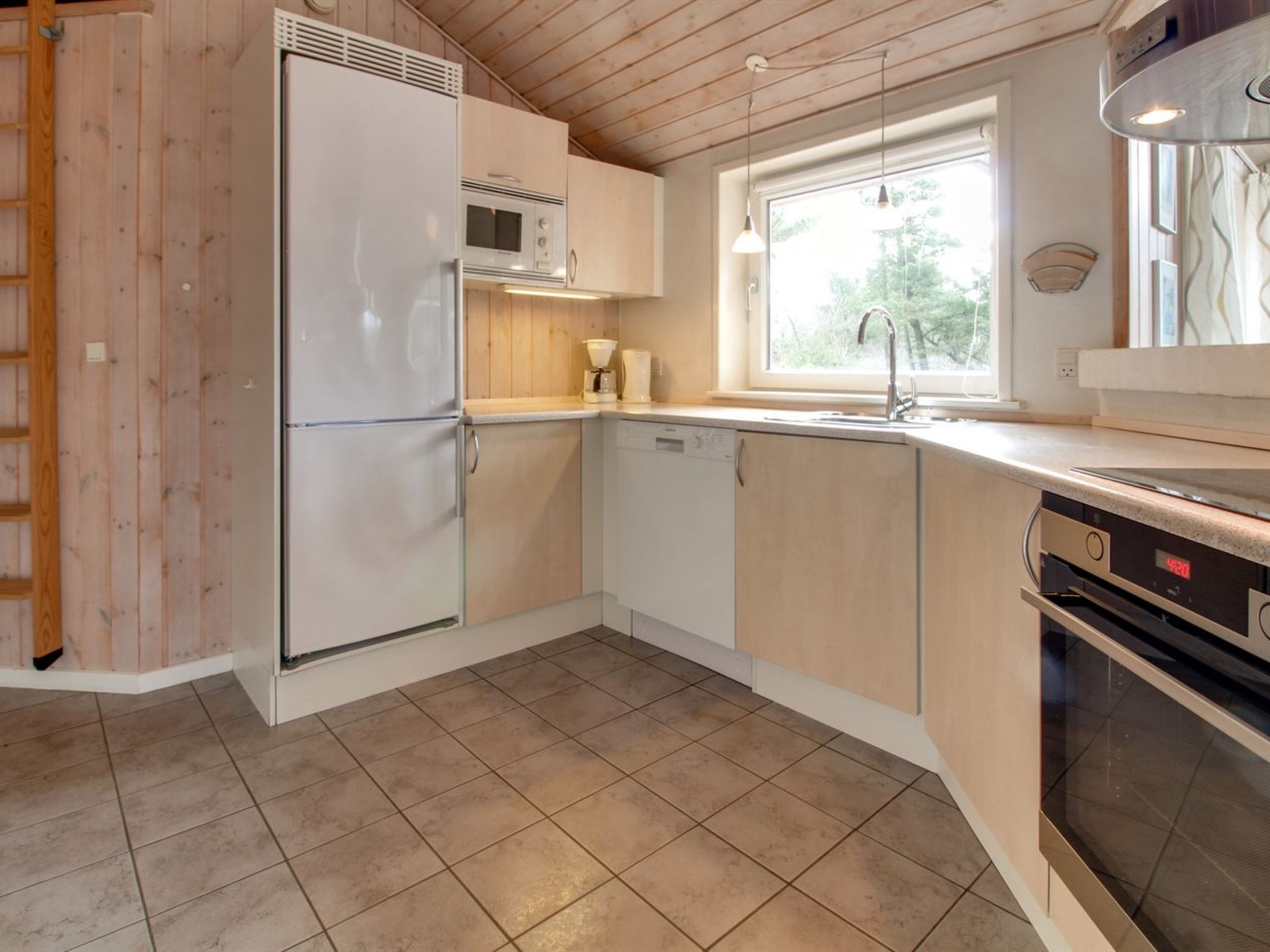 A compact kitchen with a refrigerator, microwave, dishwasher, and a window providing natural light.