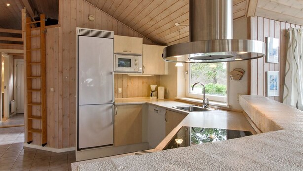 A modern kitchen with wooden paneling, a stainless steel refrigerator, a microwave, and a large window providing a view of greenery outside.