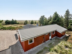 Ein eingeschossiges Holzhaus mit geneigtem Dach, einer kleinen Veranda und einem Schotterweg.