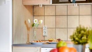 Een moderne keuken met een houten kastje, een betegelde spatwand, een vaas met bloemen, een bord muffins en een schaal fruit.