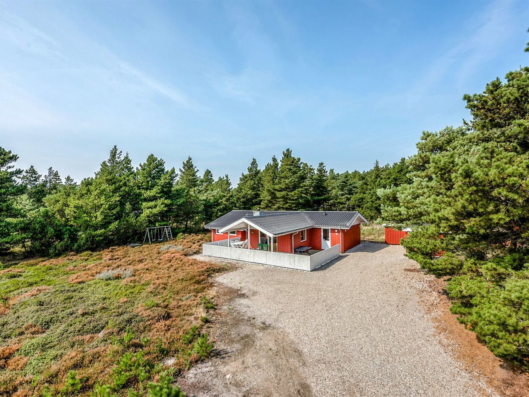 Une cabane rouge avec une allée de gravier, entourée d’une forêt dense.