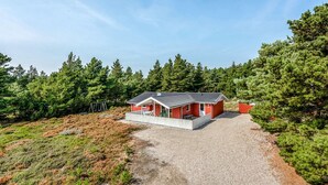 Een rode chalet met een grindpad, omringd door dicht bos.