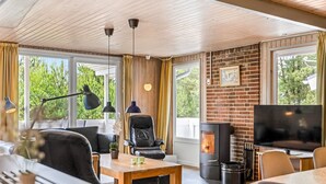 Een gezellige woonkamer met een open haard, comfortabele zitplaatsen en grote ramen met uitzicht op groen.