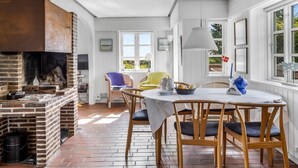 A dining area with a brick fireplace, white walls, and a view of greenery outside. - "Thorben" - 3.5km from the sea by Interhome (Rømø)