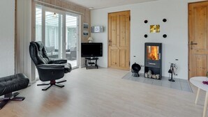 Una sala moderna con chimenea, un sillón de cuero negro, un televisor y un ventanal corredero que da a un área exterior.