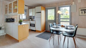 Una cocina moderna con armarios blancos, horno empotrado y microondas. Cuenta con una zona de comedor con mesa y sillas, y una ventana que ofrece vistas al exterior con vegetación.