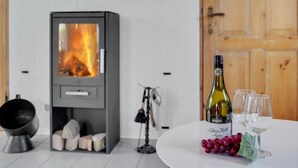 Una habitación moderna con chimenea, una mesa con botella de vino y copas, y un bol de uvas.