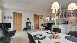 Una sala moderna con chimenea, un comedor con mesa blanca, sillas negras y una cocina con gabinetes de madera y un microondas.