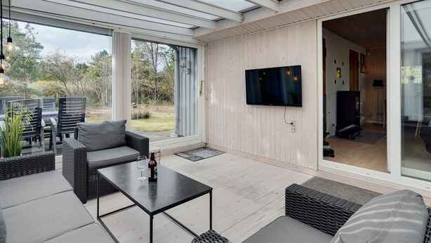 Un espacio exterior moderno con área de patio, un conjunto de sofás, una mesa y un televisor de pantalla plana montado en la pared.