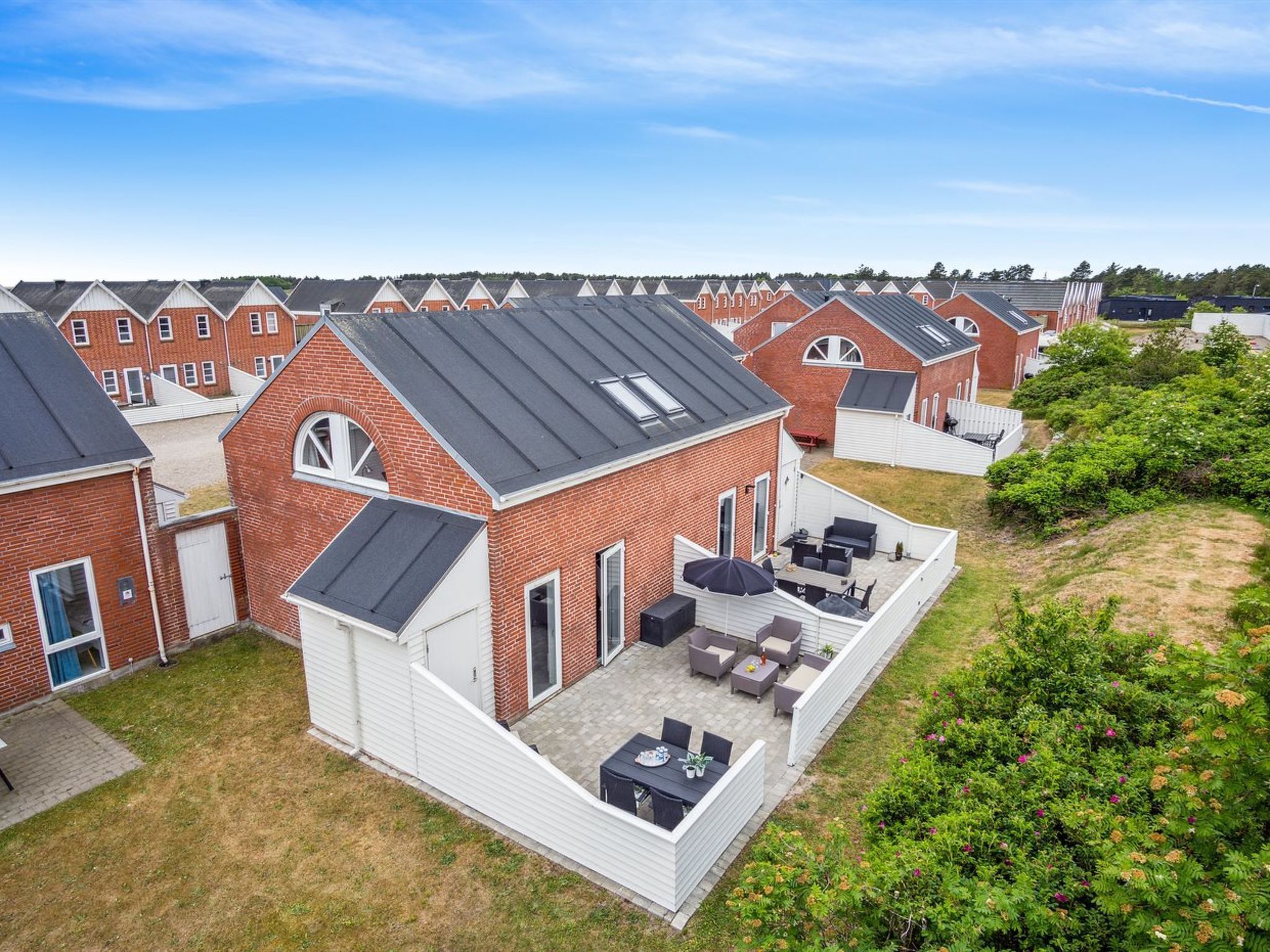 Un barrio residencial con varias casas de ladrillo, cada una con techo inclinado y un pequeño patio con mobiliario exterior.