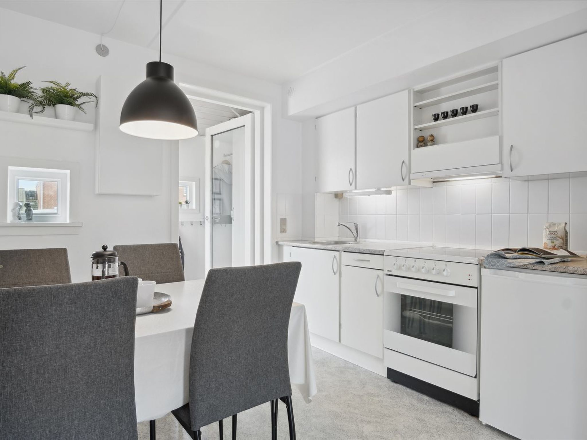 Una cocina moderna con armarios blancos, horno empotrado y un comedor con mesa y sillas.