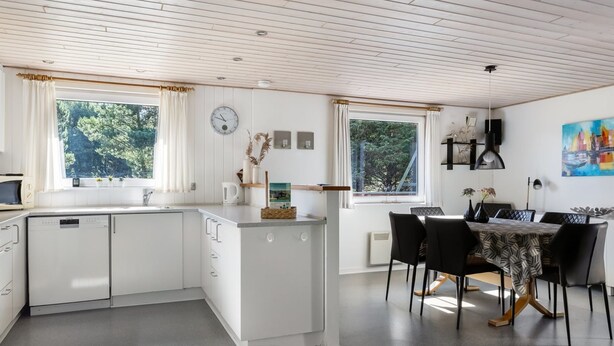 A modern kitchen with white cabinetry, a dining area with a table and chairs, and large windows offering views of greenery.