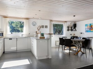 A modern kitchen with white cabinetry, a dining area with a table and chairs, and large windows offering views of greenery. - "Maija" - 1.4km from the sea by Interhome (Rømø)
