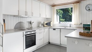 A modern kitchen with white cabinetry, a built-in oven, a microwave, and a window with curtains.