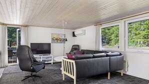 A modern living room with a grey sofa, black armchair, and a TV on a white stand.
