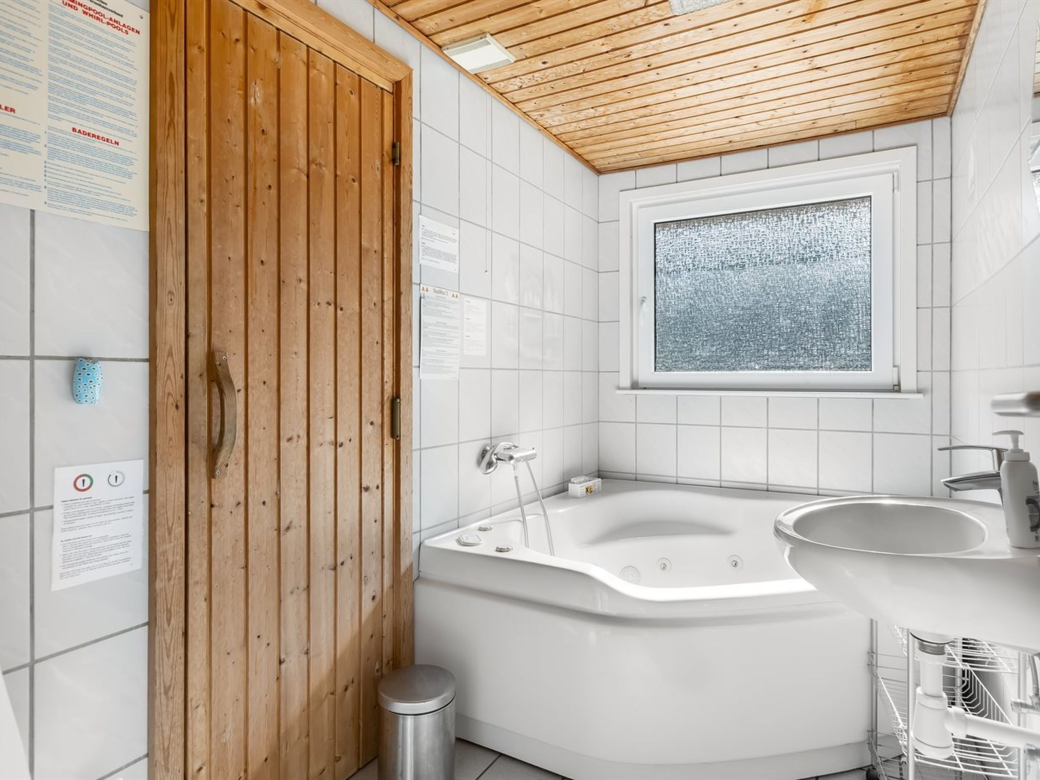 A bathroom with a wooden door, a large bathtub, a window, and a sink.