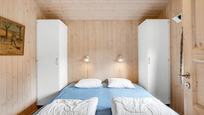 Een slaapkamer met een houten plafond, twee nachtkastjes, een bed met blauw beddengoed en twee wandlampen.