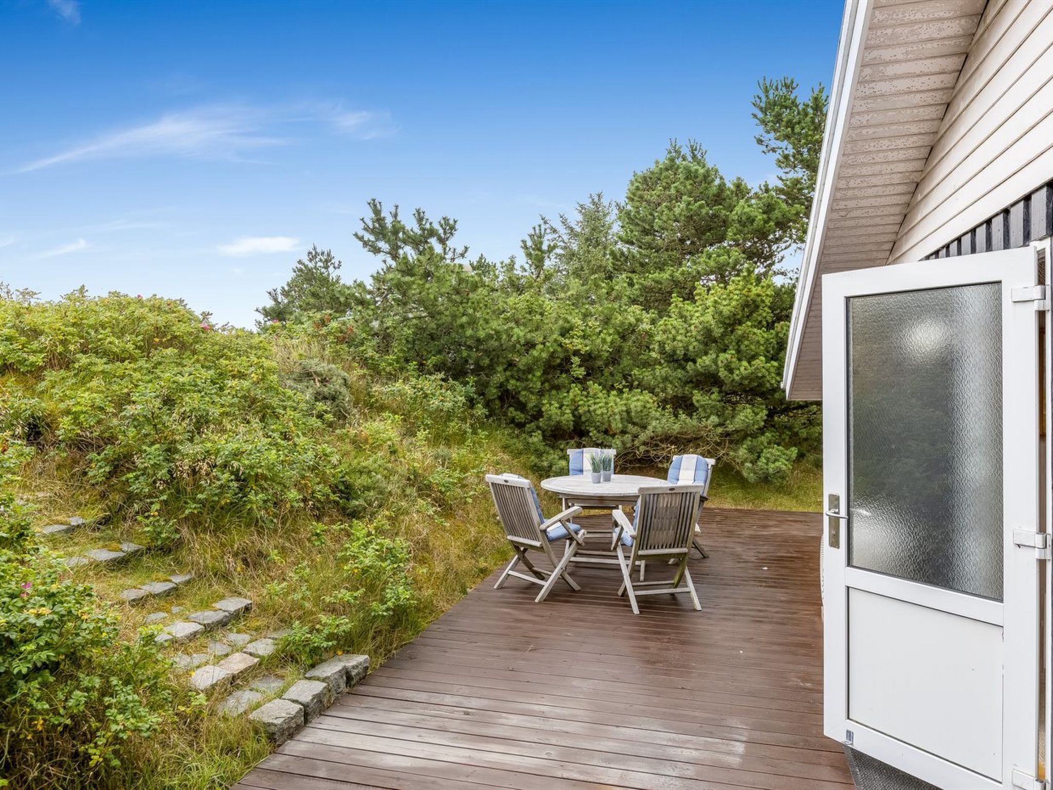 A wooden deck with a table and chairs, surrounded by greenery and trees.
