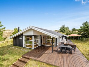Een modern huis met een ruim terras, een kamer met glazen wanden en een patio met tuinmeubilair.