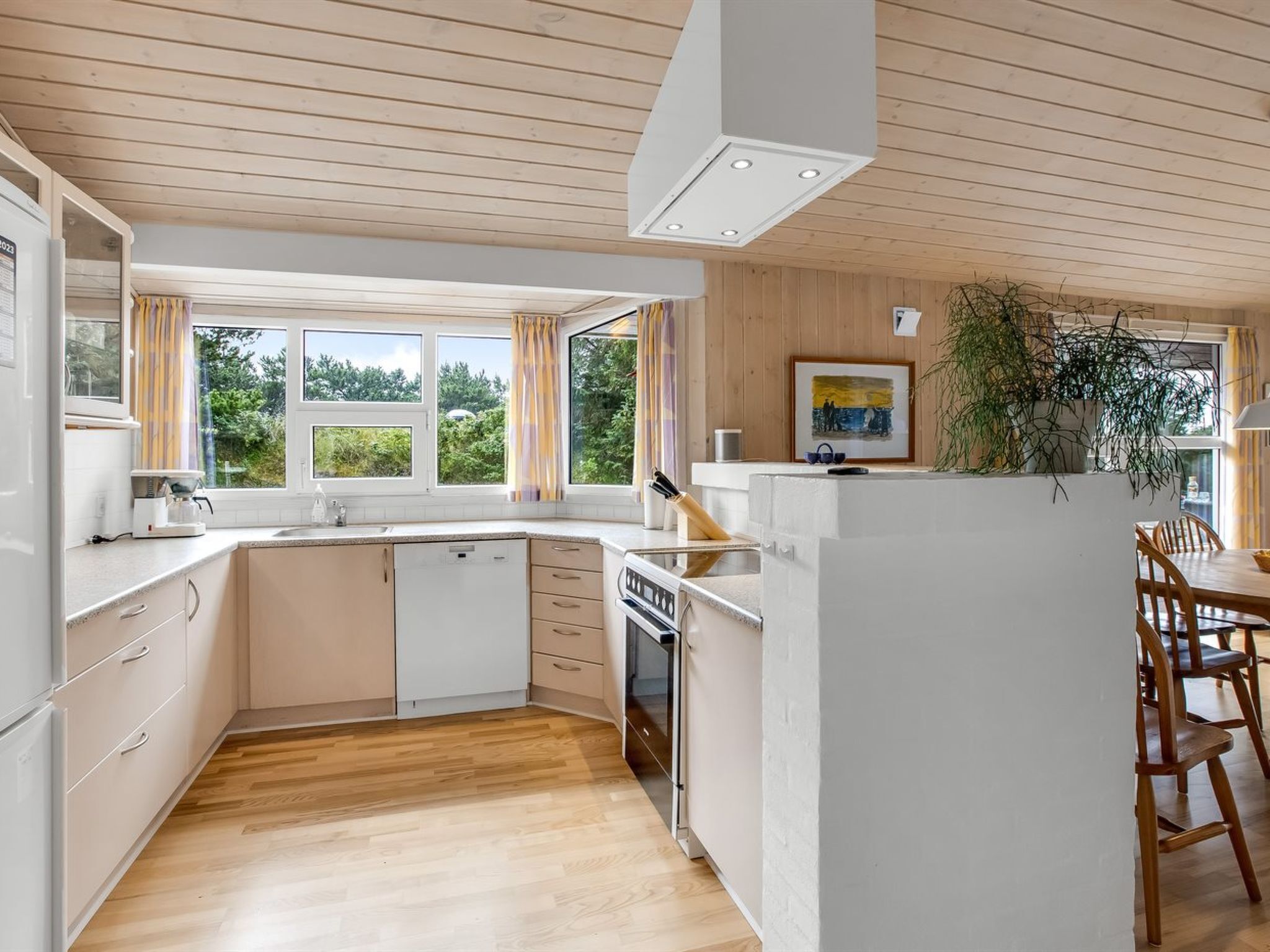 A modern kitchen with wooden flooring, white cabinetry, a built-in oven, and a dining area with wooden chairs.