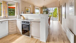 Een moderne keuken met een centraal eiland, houten vloeren en grote ramen met uitzicht op de omgeving.