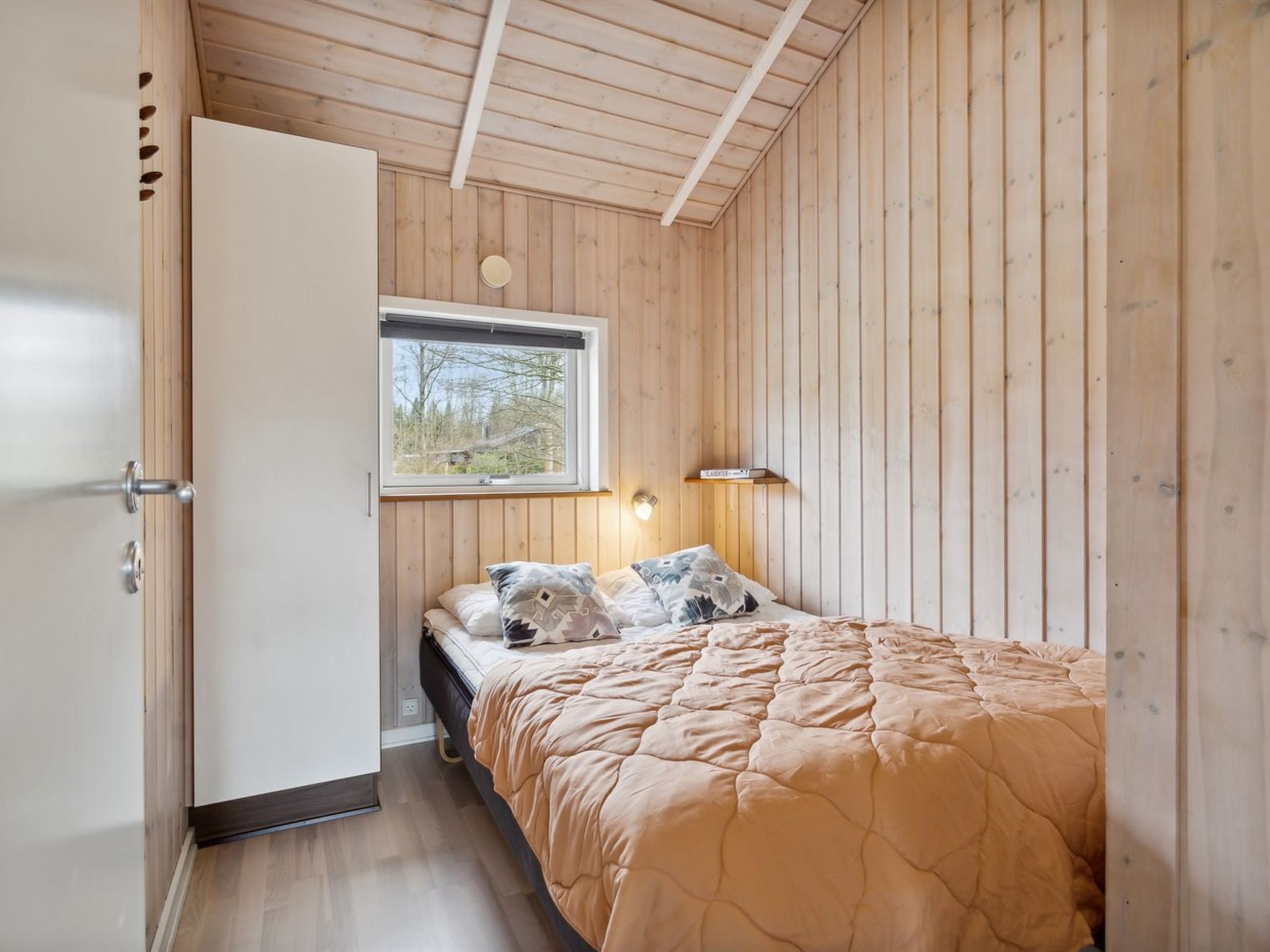 A bedroom with a bed, a window, a bedside table, and a wardrobe.