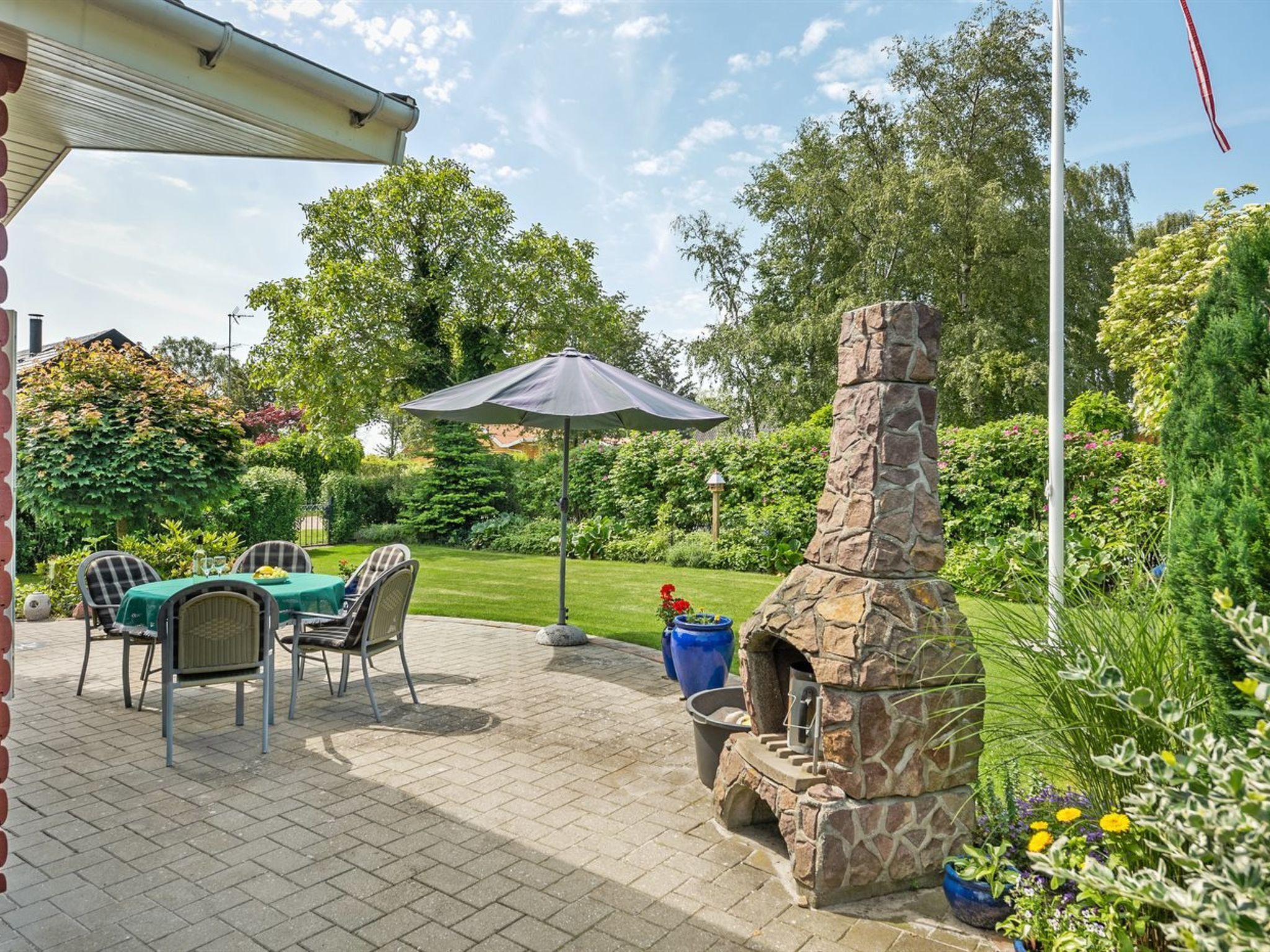 An outdoor patio with a stone fireplace, a table with chairs, and a covered umbrella.